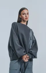 Buzo gris oscuro de cuello redondo, corte oversize y largo crop. Presenta un bolsillo grande de microfibra gris claro en el frente.
