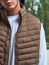 Chaleco acolchado marrón sin mangas con cuello alto y cierre lateral oculto y cremallera frontal. Bolsillos frontales y diseño plegable para fácil almacenamiento.