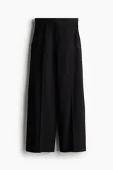 Pantalón culotte negro de tiro alto con cierre, botón y corchetes ocultos. Tiene bolsillos al bies y bolsillos traseros decorativos. Las piernas son amplias con pliegues adelante y atrás.
