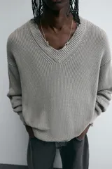 Sweater gris de punto con cuello en V, manga larga y terminaciones irregulares con efecto desgastado.