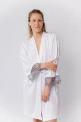 Bata tipo kimono blanca de algodón, con mangas al codo y terminación de puntilla gris. Largo por encima de la rodilla y lazo de algodón para ajustar en la cintura.