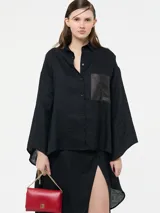 Camisa larga negra con bolsillo frontal de eco cuero, de corte suelto y mangas amplias.