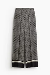 Pantalón de tiro alto con elástico en la parte posterior de la cintura y cierre oculto lateral. Presenta bolsillos discretos en las costuras laterales y piernas anchas con pliegues adelante y atrás. Diseño estampado con motivos geométricos en blanco y negro.