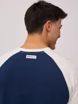 Remera azul marino con mangas raglán color crema y estampado frontal con el logo de Rusty en blanco.