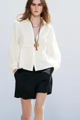 Camisa color crudo confeccionada con lino, de corte recto, cuello solapa con escote pico y manga larga. Presenta aplicación de pasamanería en el frente y cierre frontal con botones forrados a tono.
