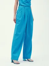 Pantalón de vestir color crema, de corte ancho y tiro alto, con pinzas delanteras y cinturón fino de cuero marrón.