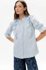 Camisa o blusa de lino color celeste claro, con cuello redondo y volado vertical que recorre el frente. Posee mangas 3/4 con volumen y puño elastizado.