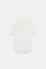 Camisa blanca de cuello solapa y manga corta, con falsos bolsillos con solapa en el delantero, bajo asimétrico y cierre frontal con botones.