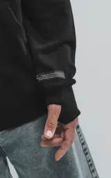 Canguro negro oversize de frisa premium con capucha ajustable y puños elastizados.