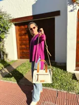 Cartera bandolera de cuero crudo con forro de tela, bolsillo frontal y bolsillo interno. Tiene correa larga regulable y manijas cortas de cuero marrón.