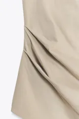 Top color beige confeccionado en algodón 100% con efecto teñido. Presenta cuello halter con lazada y escote drapeado. El bajo tiene un acabado asimétrico.