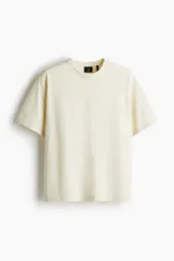 Remera color crema de punto pesado con cuello redondo ribeteado, hombros caídos y bajo recto. Corte holgado confeccionada con tejido funcional Coolmax, una fibra de poliéster de secado rápido que elimina la humedad y regula la temperatura corporal.