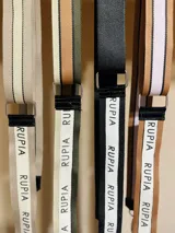 Correa de tela beige con rayas blancas y negras, con mosquetones metálicos plateados y apliques de cuero sintético negro.