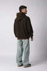 Buzo canguro negro con capucha, calce oversize, confeccionado en frisa 100% algodón con lavado gastado y aplique cosido en el pecho.