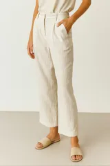 Pantalón de vestir color beige claro con finas rayas verticales en tono más oscuro. Presenta tiro alto, pinzas frontales y corte recto/holgado que termina a la altura del tobillo.
