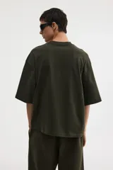 Remera de algodón pesado color verde oscuro, con cuello redondo ribeteado, hombros caídos y corte oversized.