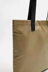 Bolso tipo shopper color beige, fabricado en tejido técnico con asas de mano de cuero negro. Tiene compartimento principal con cierre magnético y bolsillo interior con cremallera.