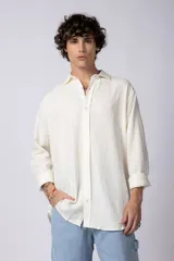 Camisa de lino color crudo, de corte amplio, con cuello clásico y mangas largas con puños abotonados.