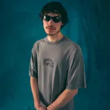 Remera gris de corte oversize con estampa en la espalda de un disco de vinilo sostenido por dos manos.