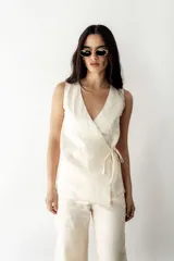 Blusa cruzada de lino color crudo, con escote en V, sin mangas y lazos laterales para ajustar.