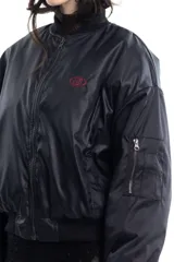 Campera bomber negra de tela satinada con cierre frontal, cuello redondo y puños y cintura elastizados. Tiene un pequeño logo bordado en el pecho y un bolsillo con cierre en la manga. Es reversible.