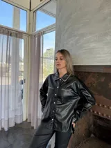 Sobrecamisa negra de cuero sintético con cuello clásico, cierre frontal con botones a presión, bolsillos con solapa en el pecho y detalle de pespuntes en contraste.