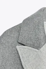 Abrigo gris de corte recto, largo hasta la rodilla, con cuello solapa, doble botonadura frontal y bolsillos con solapa.