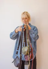 Bandolera de cuero color rojo con detalles en negro, con correa regulable y cierre superior con cremallera.