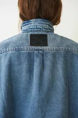 Camisa de jean celeste de manga corta, con dos bolsillos frontales, abotonada con broches a presión y cuello camisero.