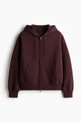 Campera con capucha de tejido pesado, color borgoña oscuro, con cierre frontal, bolsillos canguro y puños y bajo acanalados. Presenta un corte oversized y holgado.