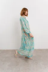 Vestido largo azul con estampado floral en tonos beige, confeccionado en viscosa. Presenta escote en V, botonadura completa en el frente y mangas largas con volados.