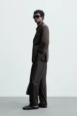 Pantalón de vestir negro de corte recto, confeccionado en tejido de algodón con acabado ligeramente encerado. Cuenta con bolsillos laterales y traseros de vivo. El cierre frontal es con cremallera y gancho metálico oculto.