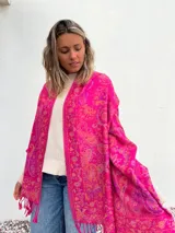 Pañuelo fucsia con estampado de arabescos en tonos naranja y violeta, con flecos en el borde.