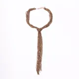 Collar tipo corbata o lazo, compuesto por múltiples hebras de pequeñas cuentas color bronce o dorado oscuro, anudadas al frente con un extremo colgante largo.