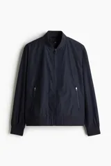 Campera bomber azul marino con cuello elevado acanalado y cierre frontal. Tiene bolsillos laterales y un bolsillo interior, todos con cierre. Los puños y el bajo son acanalados. Está forrada.
