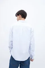 Camisa celeste con rayas verticales blancas, de corte regular, con cuello solapa clásico, bolsillo en el pecho y botones personalizados.