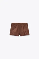 Shorts de tiro alto color negro con textura de gamuza, bolsillos delanteros y cierre frontal con cremallera y ganchos metálicos.