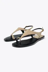 Sandalia plana color beige de cuero gamuzado, con tira entre los dedos y pulsera con hebilla ajustable.