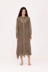 Vestido camisero largo midi de calce recto, confeccionado en tejido liviano y semitransparente, color verde oliva desgastado. Presenta cierre frontal con botones, cuello mao, mangas largas con puño y terminaciones irregulares y deshilachadas en el bajo.