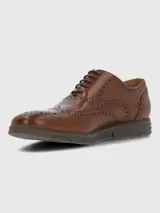 Zapato de vestir tipo Oxford o Brogue, color marrón cuero, con puntera y laterales decorados con perforaciones (broguing). Posee cordones y una suela de goma gruesa y moderna de color marrón oscuro.