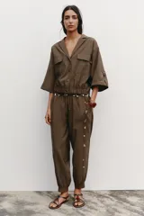 Camisa marrón de cuello solapa y manga corta con trabilla y botón. Tiene bolsillos delanteros de plastrón con solapa, bajo elástico y cierre frontal con botones a presión.