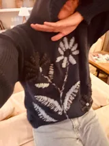 Hoodie azul marino de tejido de lana con bordado de una flor blanca en el frente.