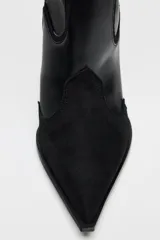 Bota alta de cuero negro con puntera fina y tacón de aguja. Diseño estilo cowboy con paneles combinados de cuero liso y gamuza.