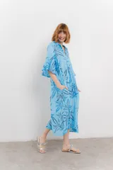 Vestido largo celeste con estampado de hojas azules, corte suelto, escote en V, mangas 3/4 amplias y bolsillos laterales.