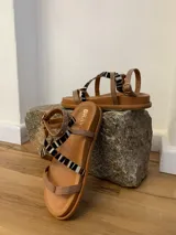 Sandalias bajas de cuero color suela con tiras de cuero y pelo animal print cebra en blanco y negro.