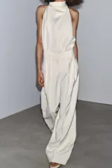 Pantalón fluido color crudo, de tiro medio con cintura con trabillas, bolsillos laterales, pinzas y raya planchada en delantero. Cierre frontal con cremallera, botón y ganchos metálicos.