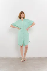 Vestido camisero corto color verde oliva, confeccionado en lino 100%. Tiene botones en la parte delantera, cuello camisero, mangas cortas con botón para arremangar y bolsillos laterales.