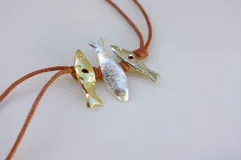 Gargantilla con hilo de algodón color camel y tres dijes de peces realizados en bronce, alpaca y plata 925.
