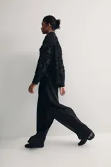 Camisa negra con textura, cuello de pico, botones delanteros, canesú con pliegues en la espalda, mangas largas con hombros caídos, puños abotonados y bajo redondeado.