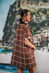 Vestido camisero corto con estampado a cuadros en tonos beige, rojo y azul. Tiene cuello camisero, botones frontales, bolsillo en el pecho y corte recto.